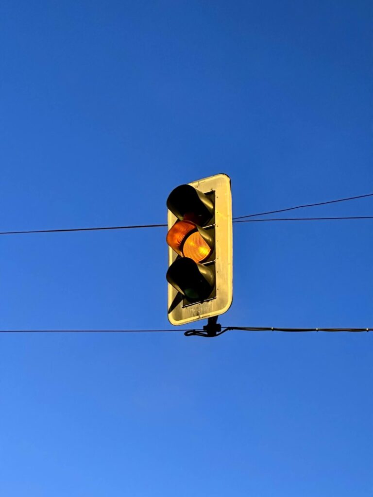 Traffic signal showing a steady yellow light against a clear blue sky, indicating the question 'what does a steady yellow light mean.